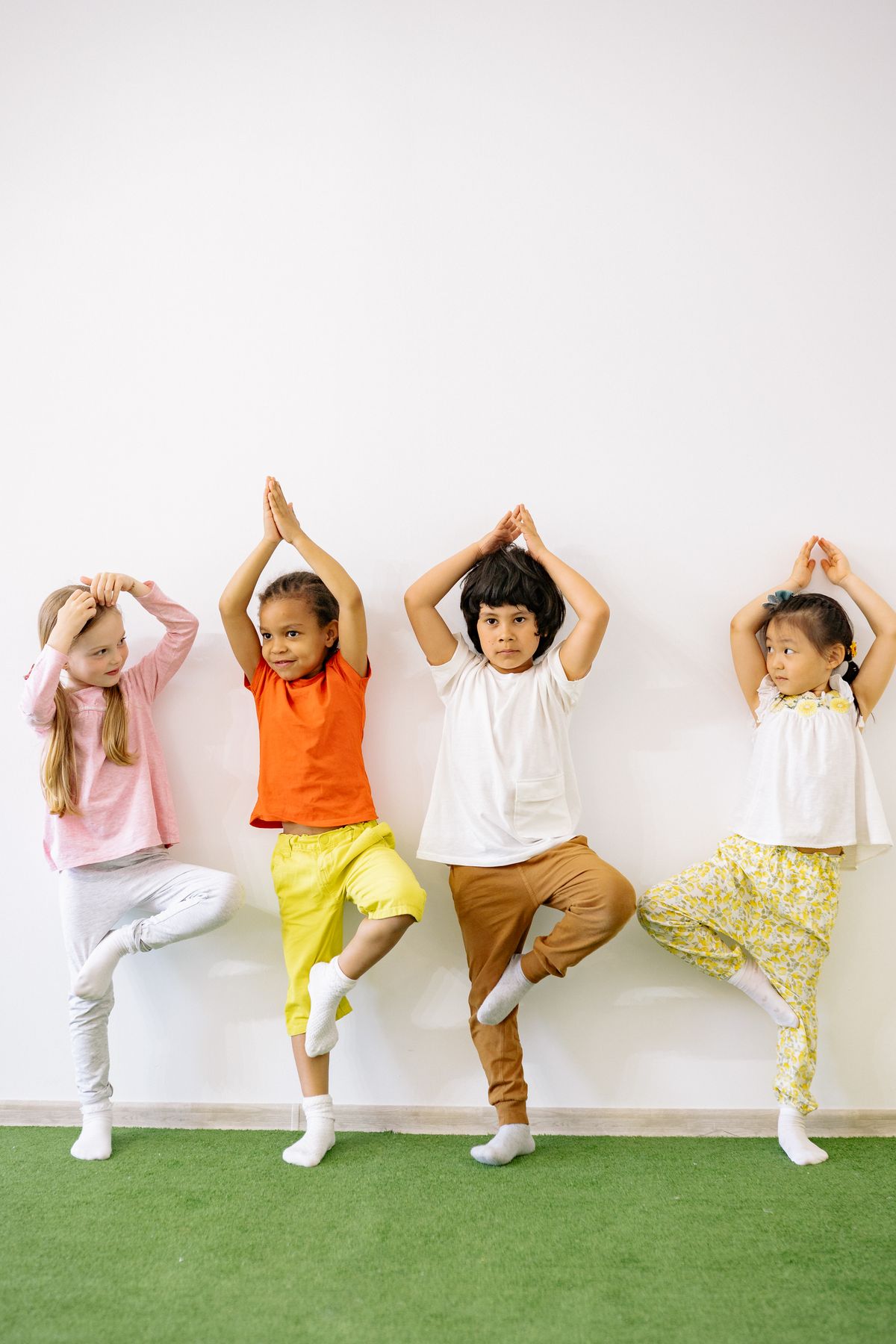 Four young children balancing on one foot with hands raised overhead