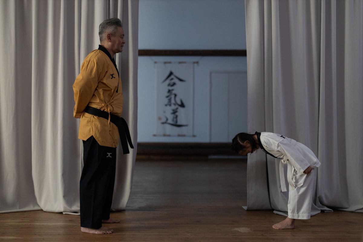 A young karate student bowing to her instructor at the edge of the mat