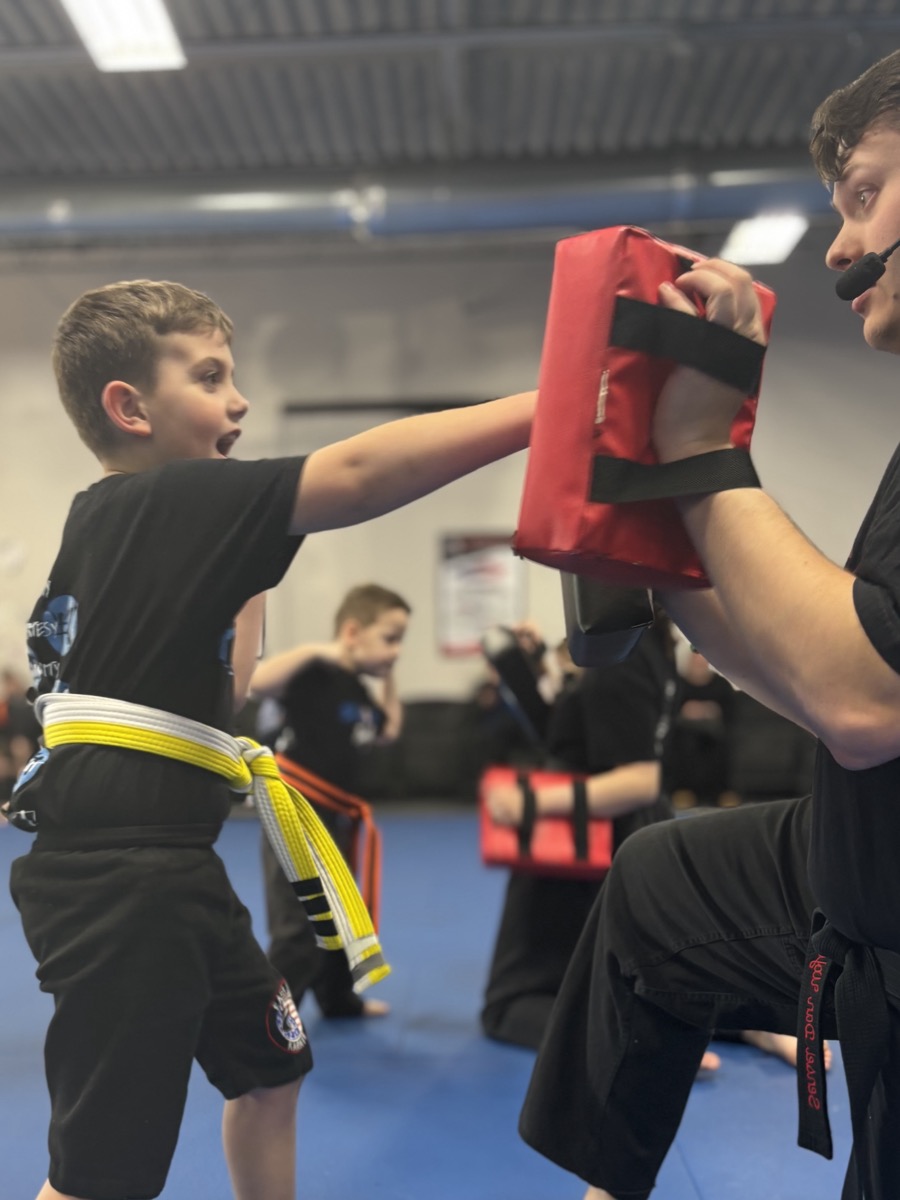 Young student practicing pad strikes with instructor at East West Karate