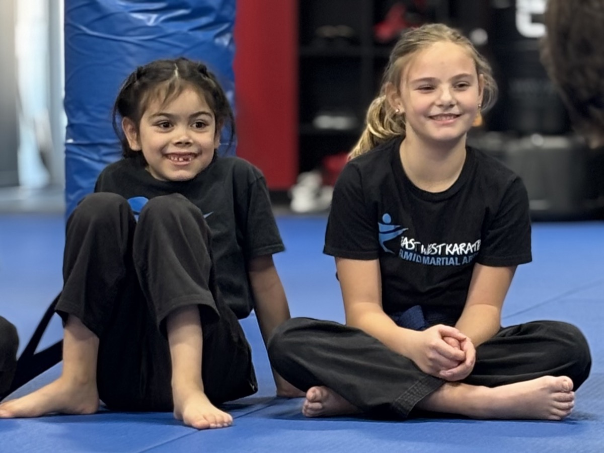 Two young students sitting on the mat smiling at East West Karate Trevose